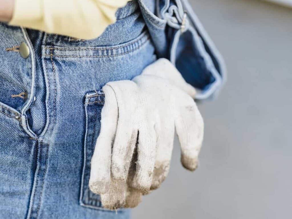 Dirty white gardening gloves in back pocket of jeans